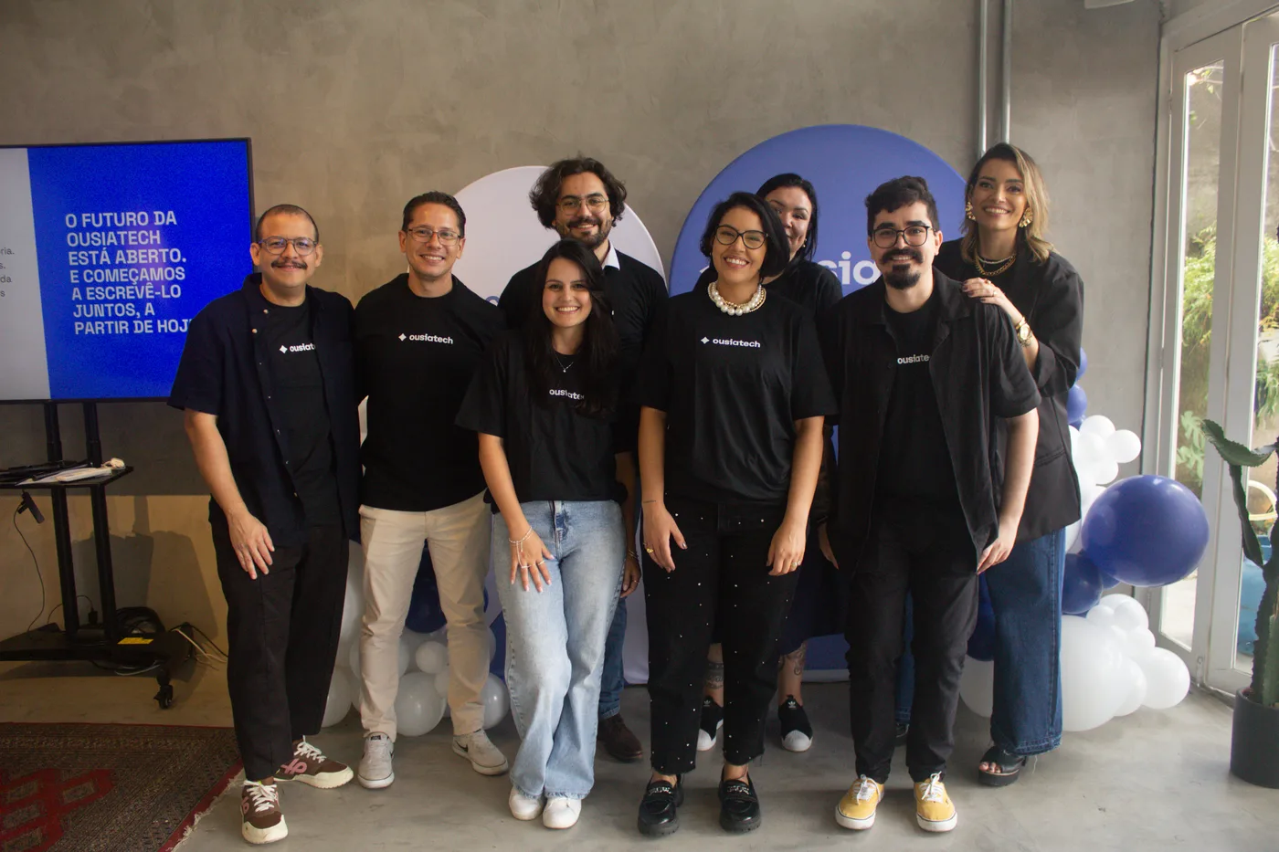 Equipe da OusiaTech reunida na confraternização de 2025, em frente ao painel com a frase O futuro da OusiaTech está aberto